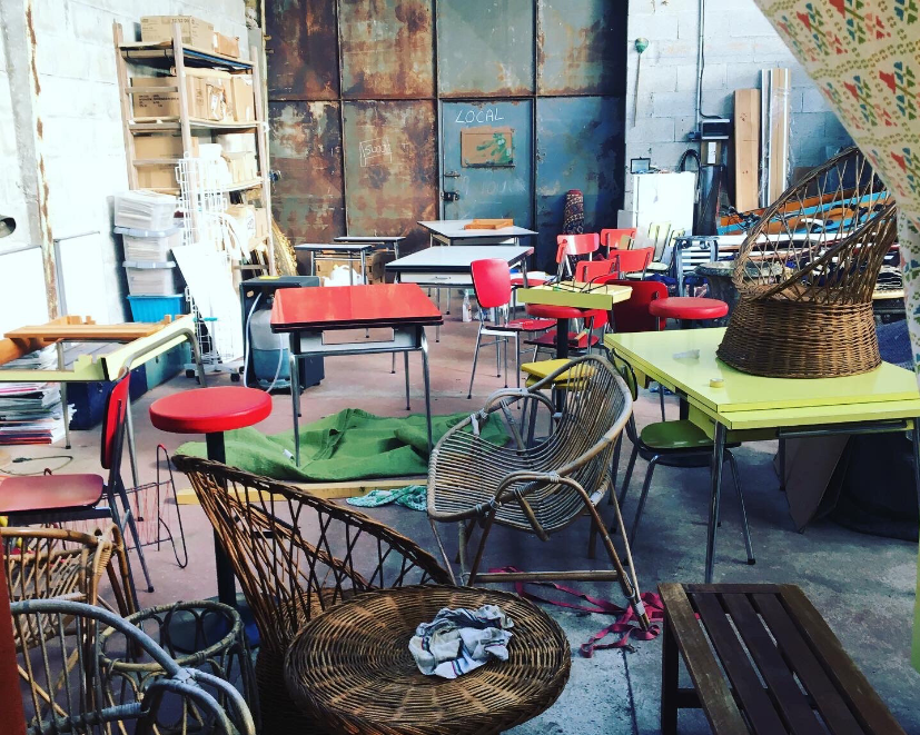 Un studio d'art encombré avec diverses chaises, tables et fournitures d'art vintage disséminées dans la pièce.